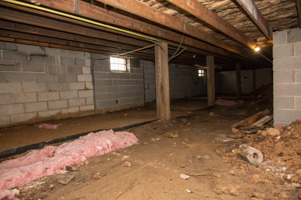 A bare-dirt crawl space with sagging insulation before cleanout and encapsulation
