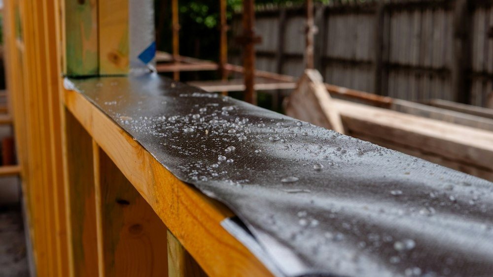 Black waterproofing membrane laid over a wall, beaded with rain