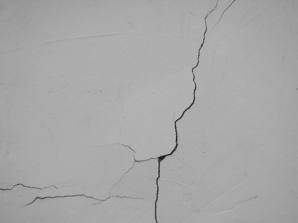 A close-up of a crack branching down a white painted basement wall